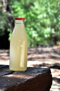 A glass bottle of homemade ginger ale on a wooden surface outdoors