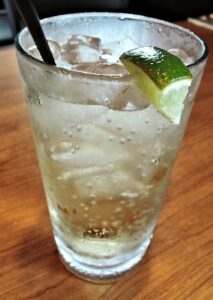 Icy glass of ginger ale with a lime wedge on a wooden table.