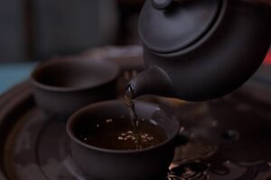 Dark teapot pouring oolong into a matching cup on a traditional serving tray.