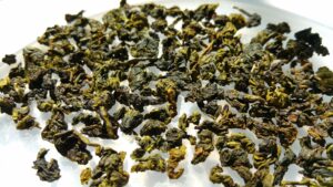 Dried oolong tea leaves spread out on a white surface, showing a mix of dark and light green hues