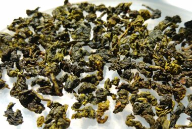 Dried oolong leaves spread out on a white surface, showing a mix of dark and light green hues