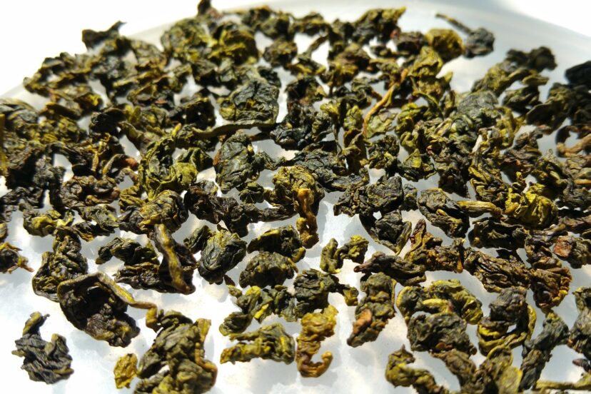 Dried oolong leaves spread out on a white surface, showing a mix of dark and light green hues