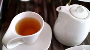 A cup of warm oolong tea beside a porcelain teapot on a wooden table."